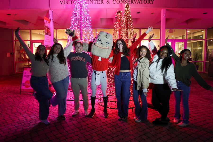 UGA students pose with Hairy Dawg in front of orange and pink illuminated trees